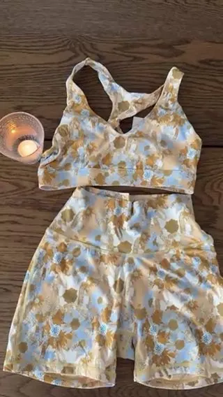 A floral two-piece activewear set laid out on a wooden floor beside a lit candle