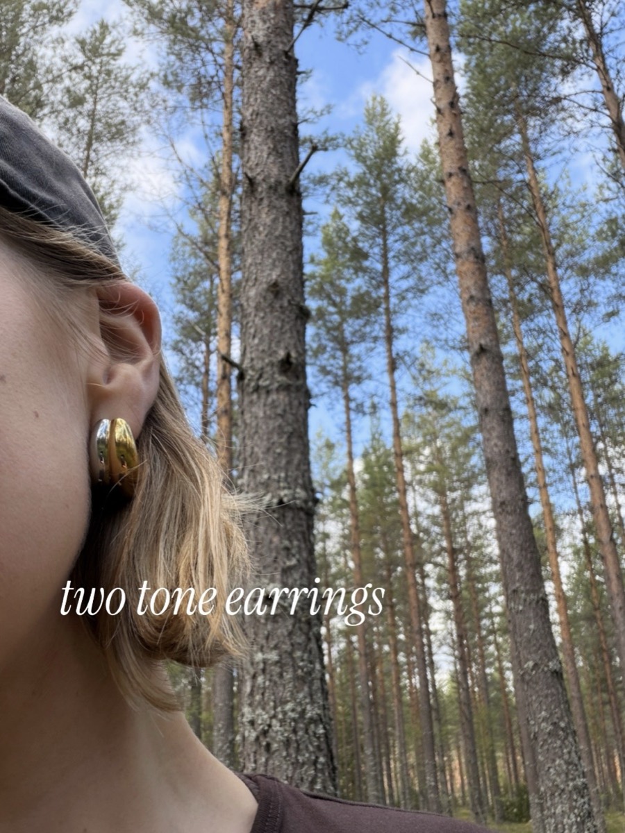 Close-up of two-tone gold and silver hoop earrings, worn outdoors among pine trees