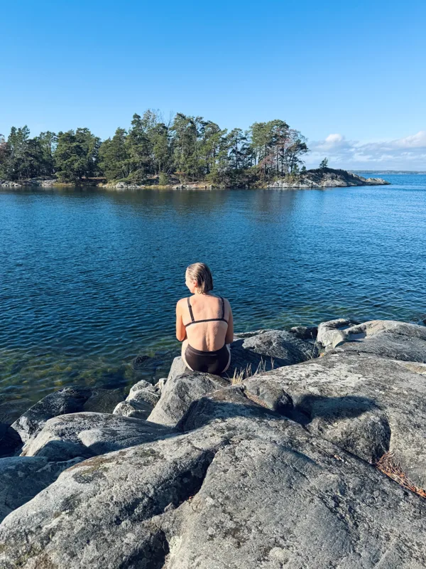 Camilla sitting on the archipelago rocks in a Tumla swimsuit, looking out over the water