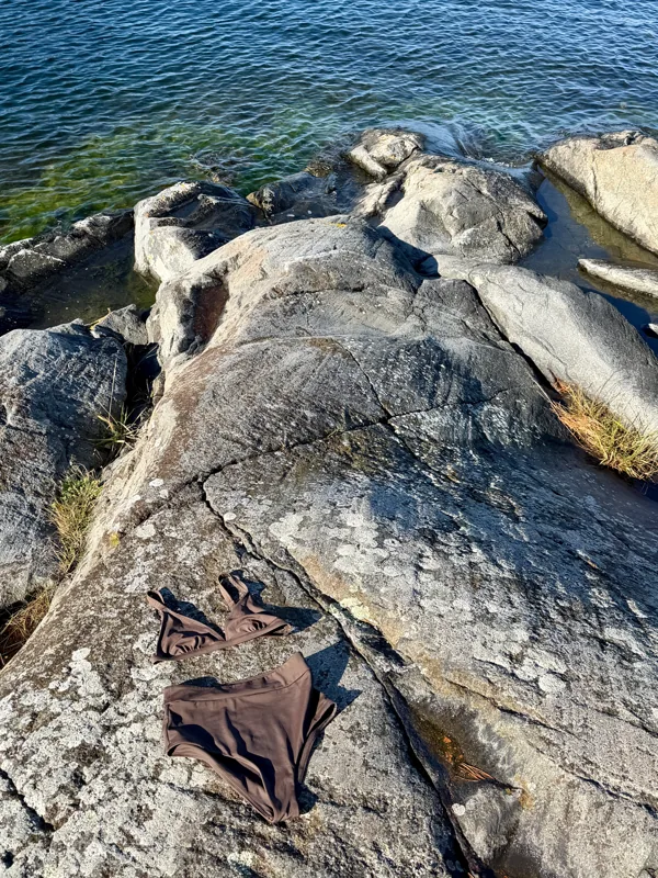 A Tumla swimsuit laid out to dry on sun-warmed rocks by the sea