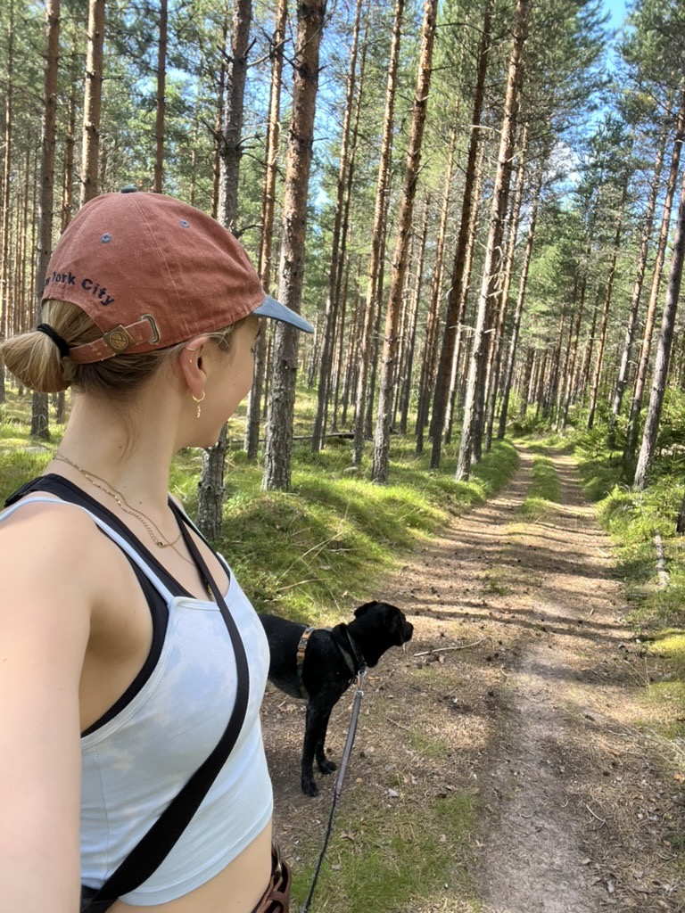 Camilla walking her dog along a sunlit forest trail