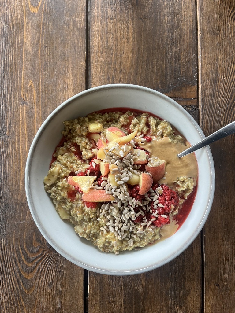 A styled porridge bowl with apple, raspberry and seeds on dark wood